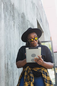 Young woman using mobile phone while standing against wall