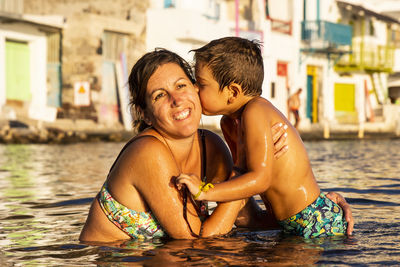 Shirtless son kissing mother in river during sunset