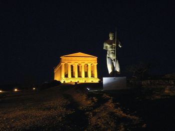 Low angle view of illuminated statue by building against sky at night