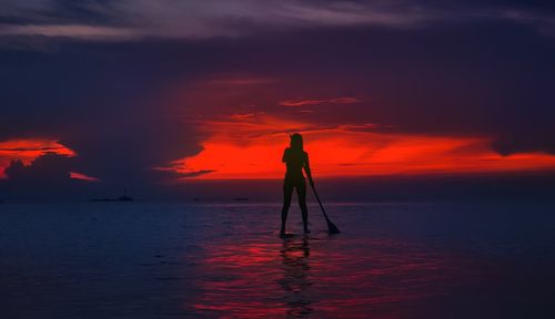 Silhouette woman standing in sea against sky during sunset