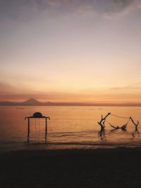 Silhouette parasols on beach against sky during sunset