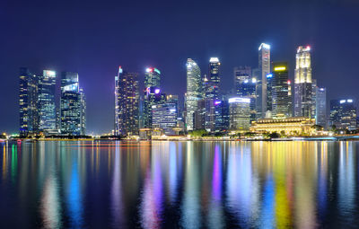 Illuminated modern buildings in city against sky at night