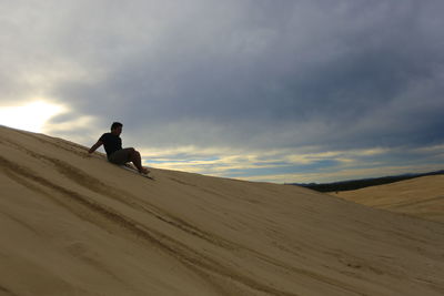 Man sitting on sand dune in desert against sky