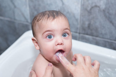 Cropped hand of mother cleaning toddler son mouth in bathtub