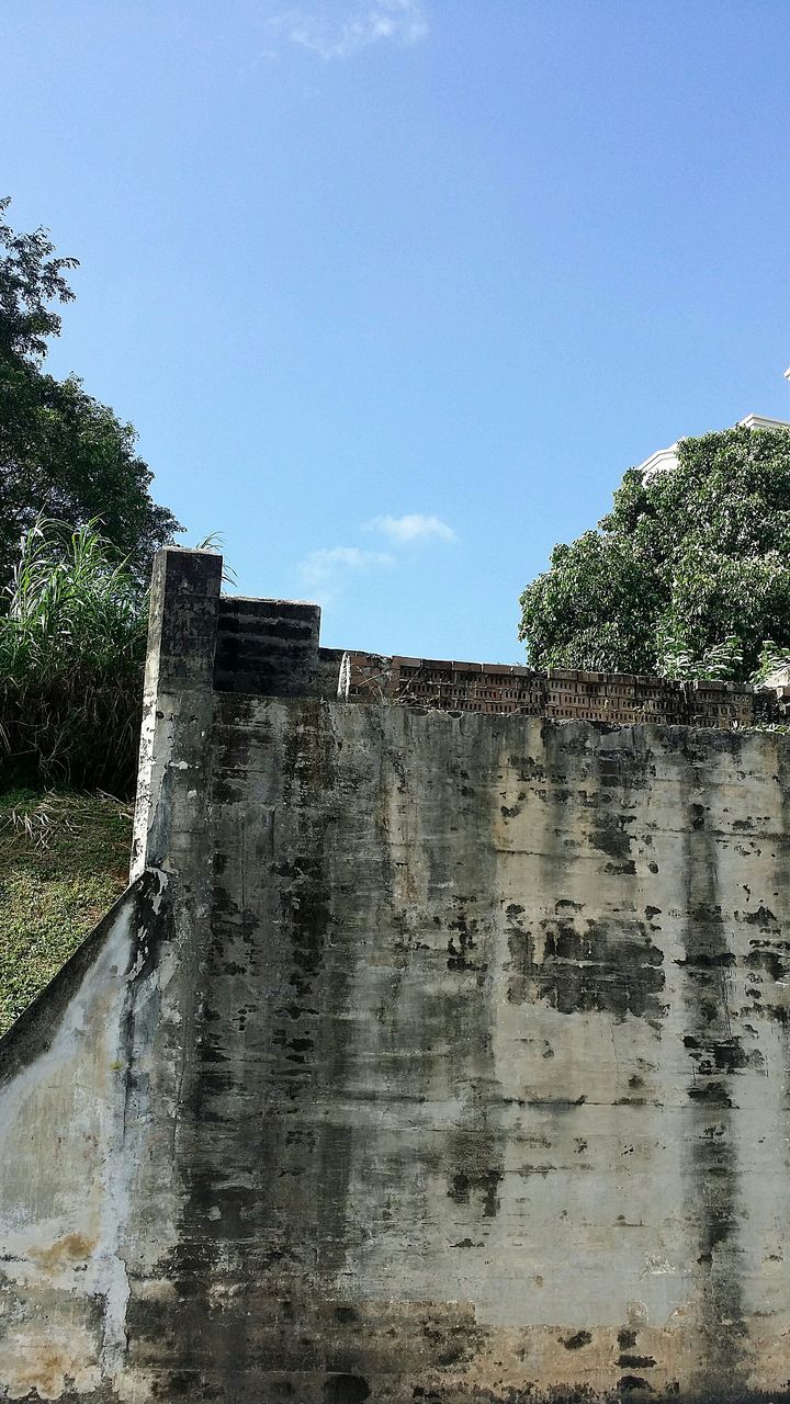 architecture, built structure, building exterior, clear sky, low angle view, blue, wall - building feature, sky, stone wall, day, old, outdoors, tree, stone material, wall, sunlight, weathered, no people, history, copy space