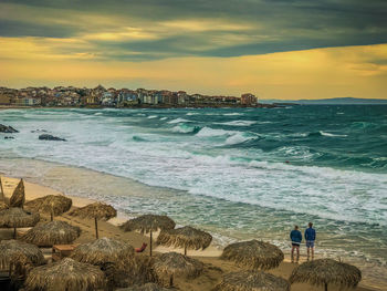 People at beach against sky during sunset