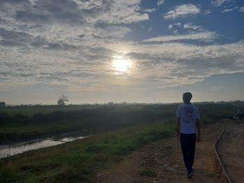 Rear view of man standing on field against sky during sunset