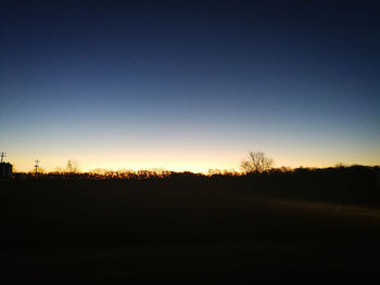 Silhouette trees on field against clear sky at sunset