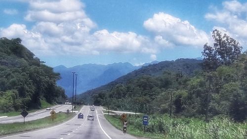 Road amidst trees and mountains against sky