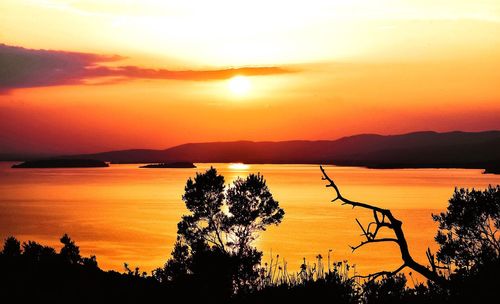 Scenic view of calm lake against dramatic sky during sunset