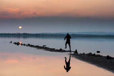 Silhouette man on shore against sky during sunset