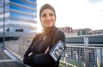 Portrait of young woman standing against railing in city