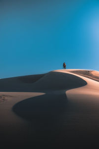 Man on sand dune in desert against clear blue sky