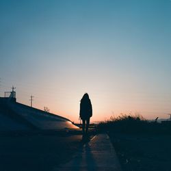 Rear view of woman standing on road at sunset