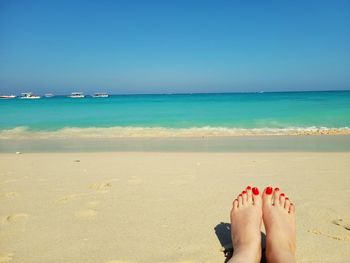 Low section of woman on beach against clear blue sky