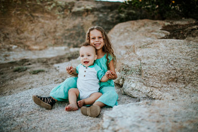 Happy young siblings sitting together on rock smiling