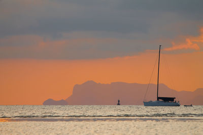 Silhouette sailboats on sea against orange sky