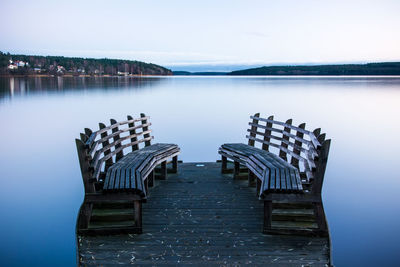 Empty chairs by lake against clear sky