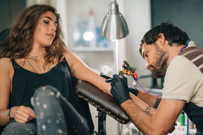 Artist making tattoo on woman hand at studio