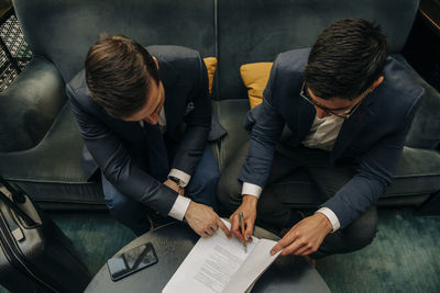 High angle view of businessman signing contract sitting by colleague at hotel lounge