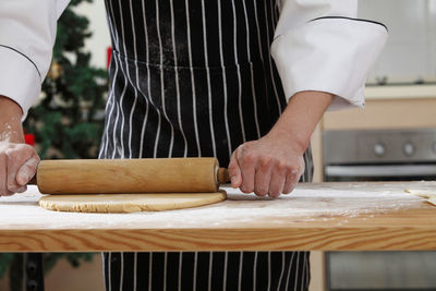 Midsection of chef rolling dough at table