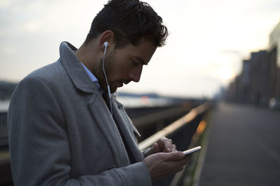 Businessman using mobile phone while standing against railing