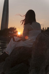 Woman sitting on rock against sky during sunset