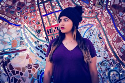 Young woman looking away while standing against mosaic wall