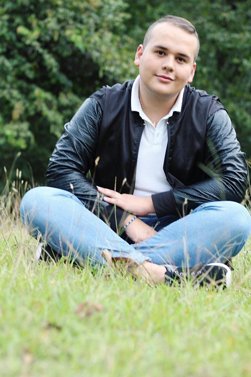 plant, young adult, grass, young men, sitting, casual clothing, one person, leisure activity, lifestyles, full length, nature, day, real people, land, looking at camera, portrait, field, relaxation, outdoors, jeans, contemplation, teenager