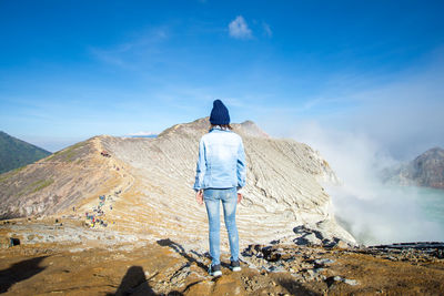 Rear view of man standing on mountain against sky