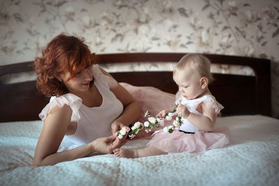 Gentle red-haired mother with a wreath of flowers and a daughter toddler in the bedroom, 