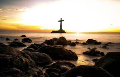 Religious cross on sea against sky during sunset