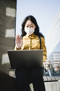 Businesswoman with face mask waving during video chat