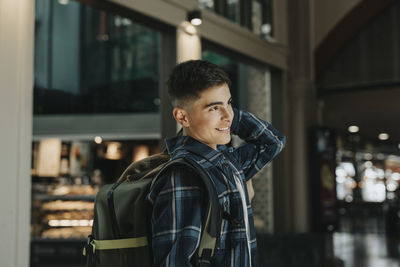 Smiling teenage boy carrying luggage while standing at station