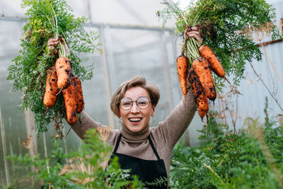 Portrait of young woman with arms raised standing amidst plants