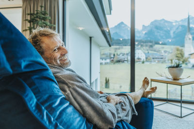 Side view of man sitting on chair by window