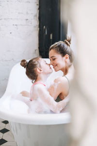 Young mother woman and little tween girl daughter having fun in bath with foam at home