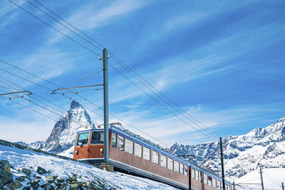 Red train running towards gornergrat station on snowy mountain against sky