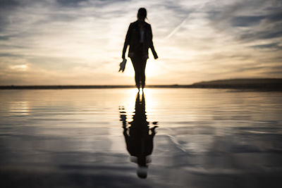 Silhouette man standing on beach against sky during sunset