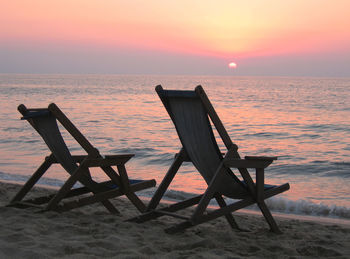 Chair on beach against sky during sunset