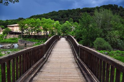 Footbridge amidst trees against sky
