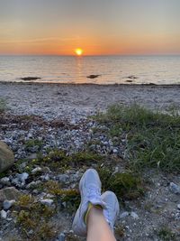 Low section of person on beach against sky during sunset