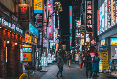 People walking on illuminated street amidst buildings at night