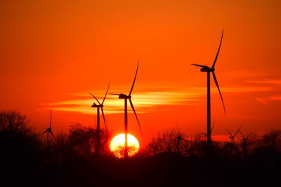 Silhouette wind turbines on field against orange sky