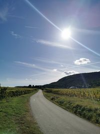 Empty road amidst field against sky