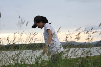 Side view of boy standing on field against sky