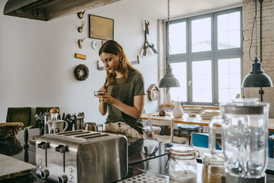 Young female entrepreneur preparing coffee while standing by counter in studio