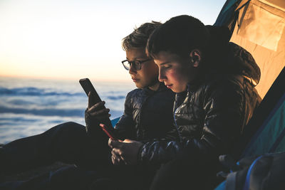 Brothers using mobile phone while camping during sunset