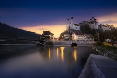 Bridge over river against buildings at sunset