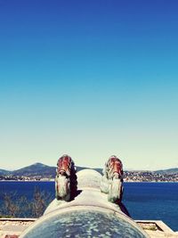 Low section of person by sea against clear blue sky